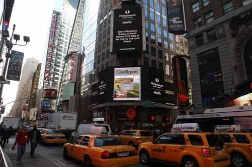 Yellow taxis and buses fill a busy street in Times Square, New York City, surrounded by tall buildings with bright digital billboards and advertisements. Amid the urban bustle, there’s no sign of cattle ranch or recreational land nearby as pedestrians walk along the sidewalks.