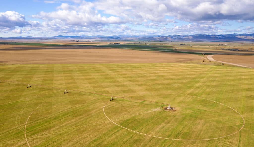 Aerial view of a large agricultural field with circular irrigation patterns, ideal recreational land or hunting property, surrounded by open plains and distant hills under a partly cloudy sky.