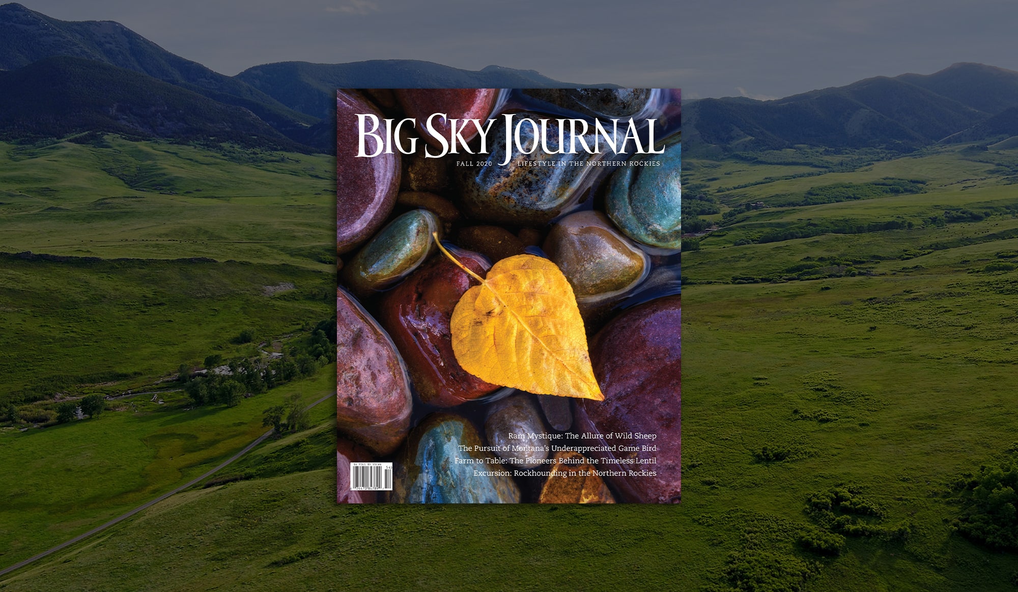 The cover of Big Sky Journal Fall 2023 features a yellow aspen leaf on smooth, colorful river stones, set against recreational land with rolling hills and mountains beneath a cloudy sky.