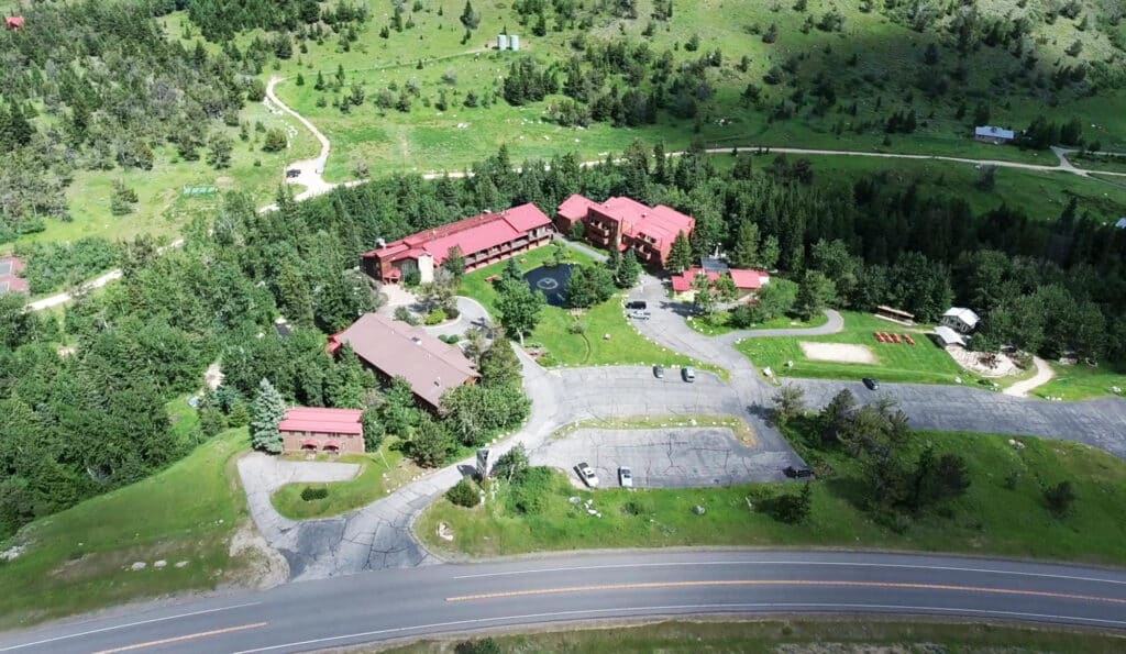 Aerial view of a lodge complex with red-roofed buildings nestled among trees and greenery, adjacent to a road with parking areas and pathways—a perfect setting for a hunting property or cattle ranch.