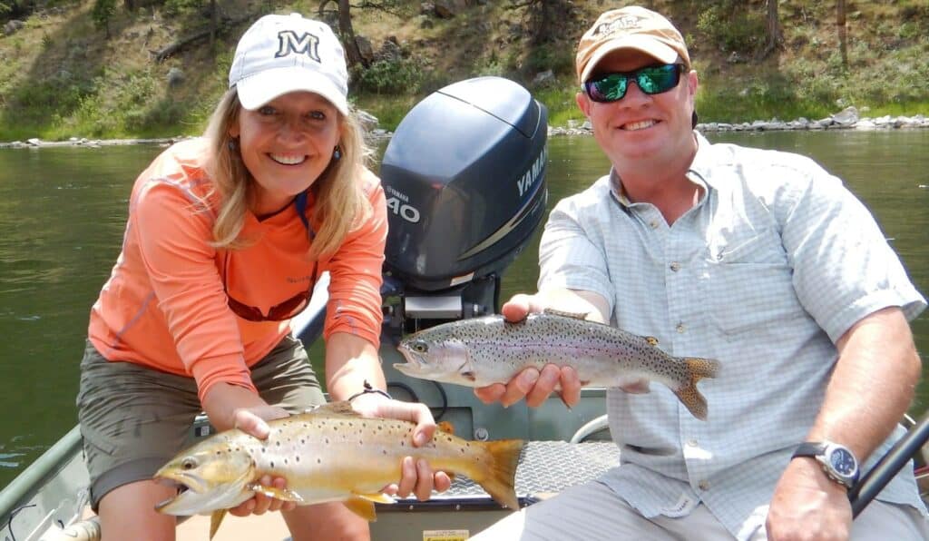 A smiling woman and man in caps sit in a boat, each proudly holding a fish they caught. Surrounded by trees and water, their fishing trip showcases the appeal of recreational land perfect for outdoor enthusiasts.