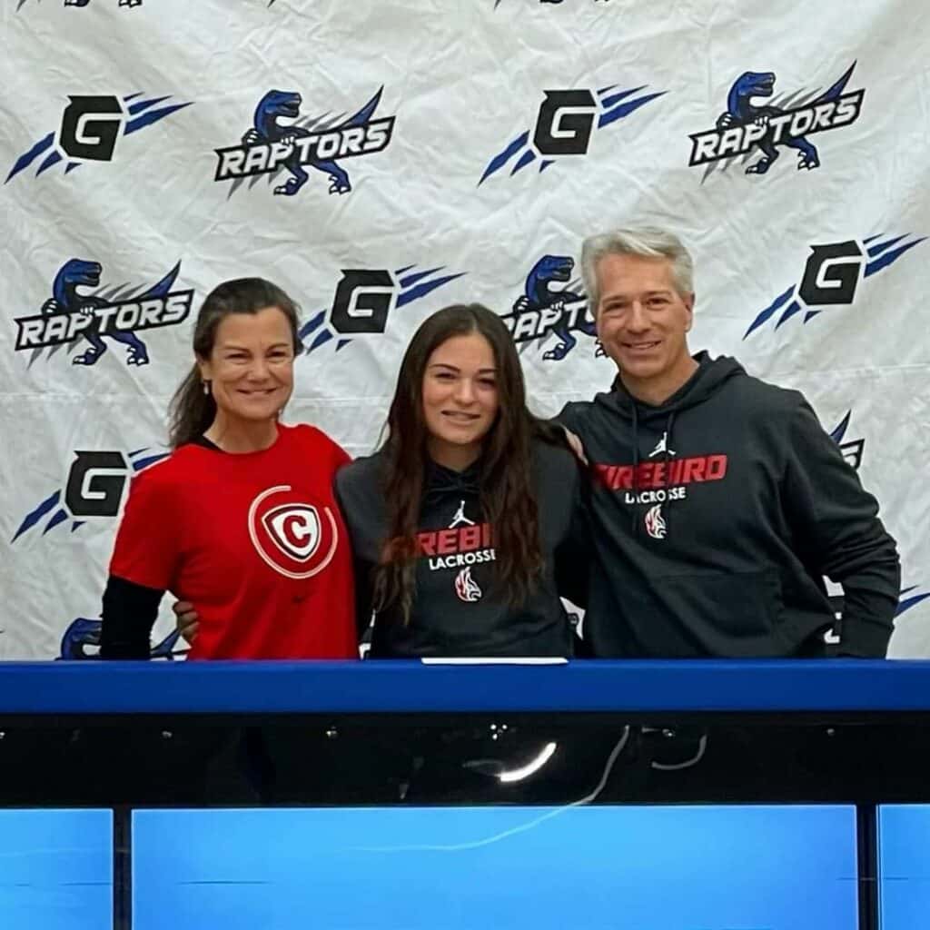 Three people stand smiling in front of a white Raptors-branded backdrop. The two adults flank a young woman at a table, all wearing sports shirts. Their image reflects on the table—a team spirit reminiscent of finding perfect recreational land or cattle ranch.