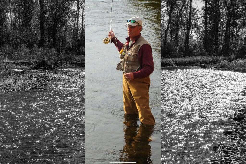 A person wearing waders, a vest, and a cap stands fly fishing in a river on recreational land for sale. The central area is in color, while the surroundings are black and white.