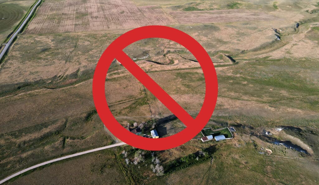 Aerial view of a rural landscape with fields and buildings, overlaid by a large red prohibition symbol, indicating restricted access to this recreational land or hunting property.