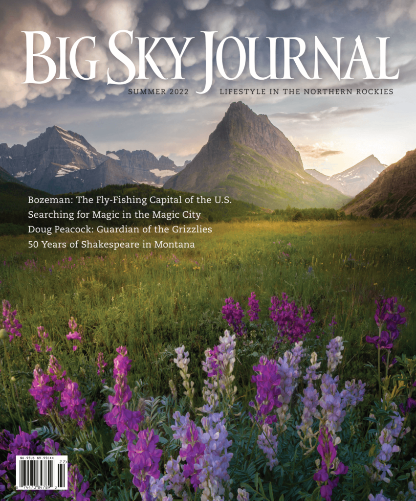 Cover of Big Sky Journal magazine featuring wildflowers in the foreground and majestic mountains under a cloudy sky, with text highlighting fly-fishing, grizzlies, Shakespeare in Montana, and the allure of land for sale in the region.