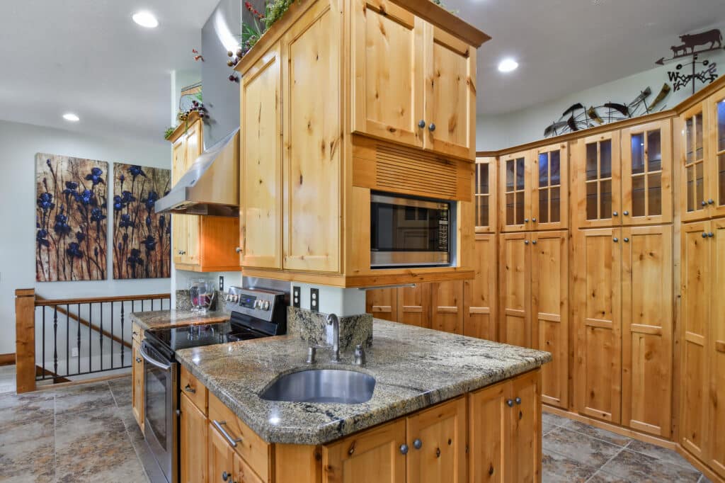 A kitchen with light wood cabinets, granite countertops, a stainless steel oven and stove, built-in microwave, small sink, tiled floors, and a decorative painting—perfect for those seeking a ranch for sale or recreational land opportunity.