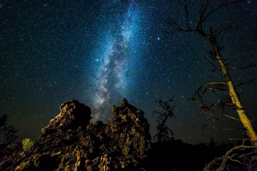 The Milky Way stretches brightly across a star-filled night sky above jagged rock formations and leafless trees silhouetted in the foreground, showcasing the beauty of this exceptional hunting property.