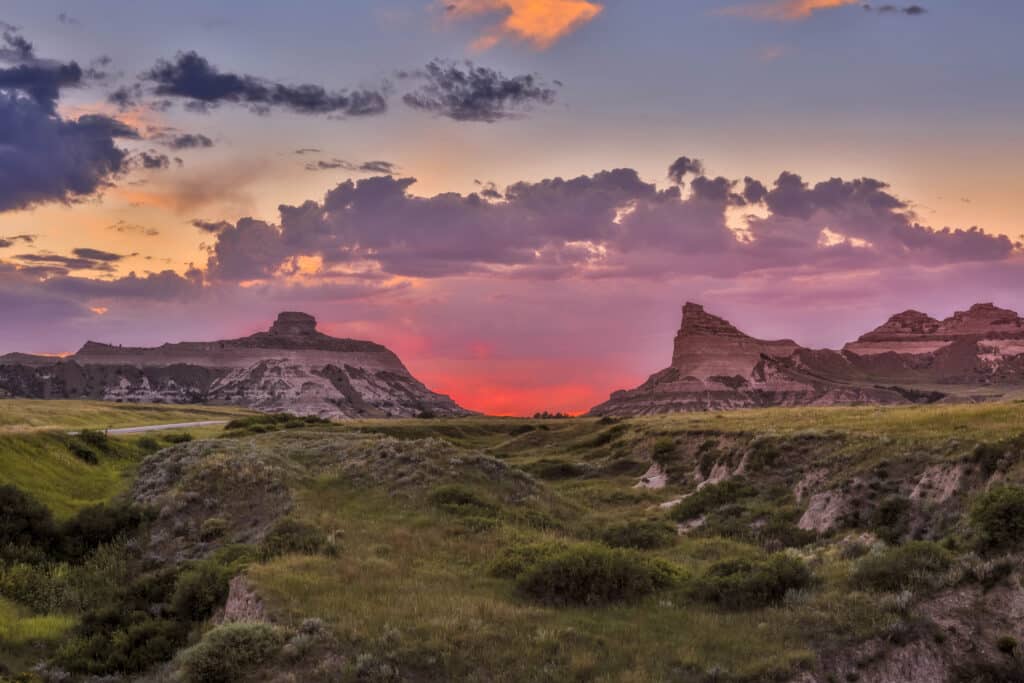 Grassy hills and rugged rock formations at sunset, with a colorful sky of orange, pink, and purple clouds—ideal recreational land or hunting property.
