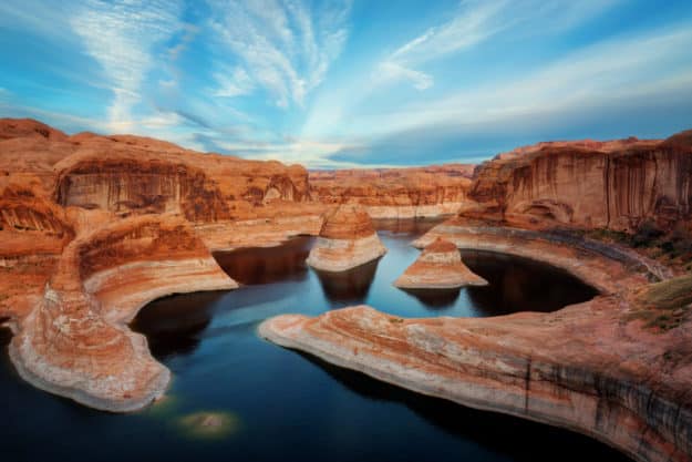 A scenic view of a winding river with dark blue water flows through red sandstone rock formations and buttes beneath a vibrant, partly cloudy sky—perfect recreational land or ranch for sale.