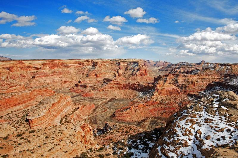 A sweeping view of a deep, winding canyon with red rock cliffs, sparse green vegetation, and patches of snow under a bright blue sky—ideal recreational land or cattle ranch opportunity.