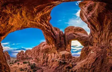 Red rock arches and formations frame a vivid blue sky with scattered clouds in a desert landscape, capturing the dramatic textures and colors typical of a scenic hunting property or cattle ranch in Utah.