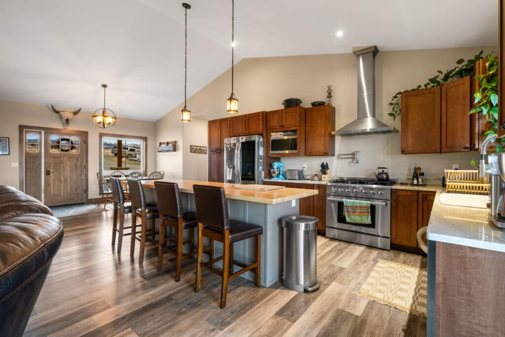 Modern kitchen at 380 Mill Gulch Road with wooden cabinets, stainless steel appliances, an island with barstools, pendant lights, and a cozy dining area. Open layout features wood flooring, large windows for natural light, and a wall-mounted bull skull decor.