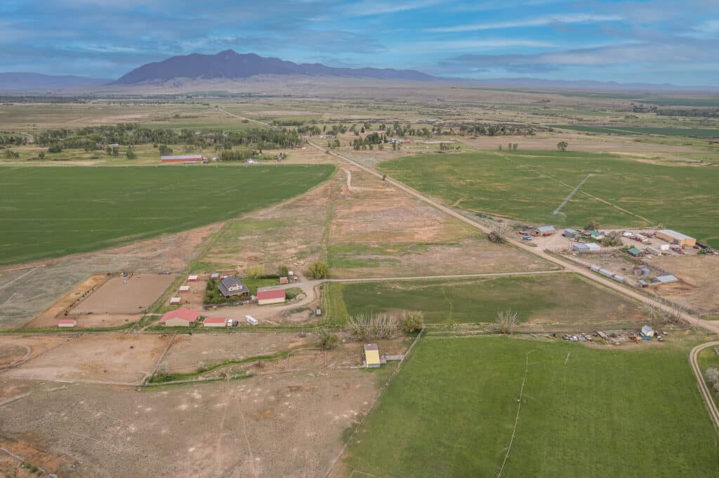 Aerial view of a rural landscape featuring green fields, scattered farm buildings along 868 Middle Road, dirt roads, and distant mountains under a blue sky with some clouds.
