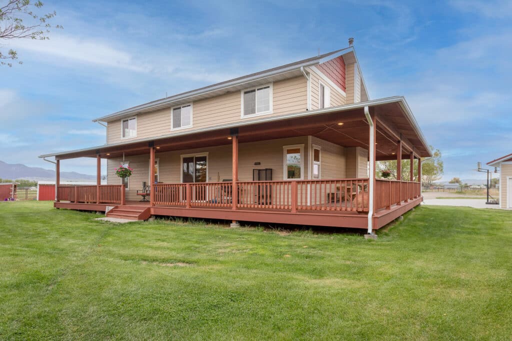 Charming two-story beige house at 868 Middle Road, featuring a large red wraparound porch with railings and hanging plants, a green lawn, and blue sky. Enjoy stunning mountain views in the distance.