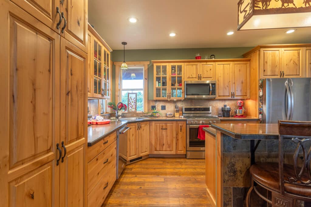 Warm, rustic kitchen at 868 Middle Road with wooden cabinets, stainless steel appliances, and a large window above the sink. The space features a built-in oven, microwave, dishwasher, and an island with seating.