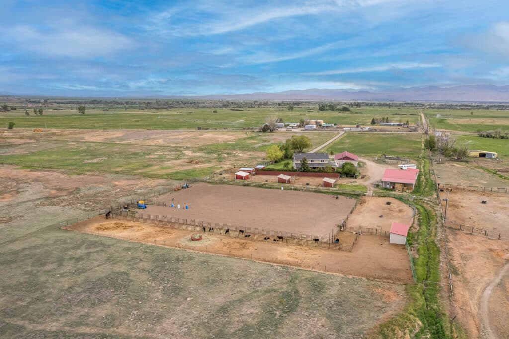 Aerial view of 868 Middle Road, a rural property featuring fenced horse arenas, several red-roofed barns, green fields, and distant mountains under a partly cloudy blue sky.