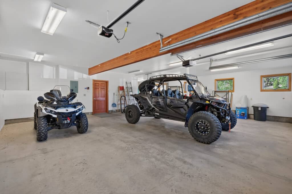 A spacious garage with a black all-terrain vehicle and a black side-by-side utility vehicle parked inside—perfect for trips to the Elkhorn sanctuary. Various storage items and tools are visible along the walls.
