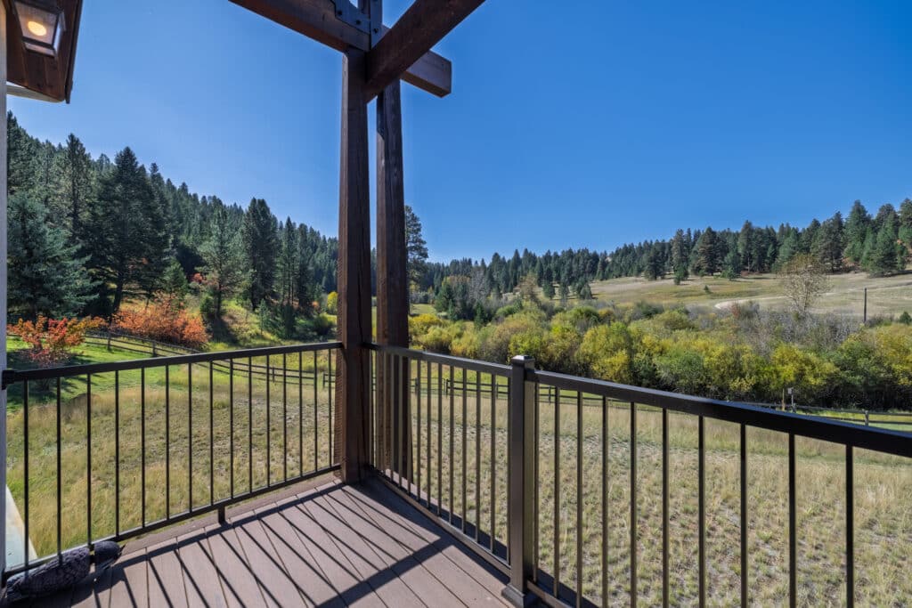 View from a wooden balcony with metal railings, overlooking a grassy field and forested hills at Elkhorn sanctuary under a clear blue sky.