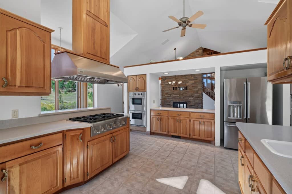 Spacious kitchen with wooden cabinets, stainless steel appliances, center island, tiled floor, and vaulted ceiling with a fan. Enjoy natural light and serene views—your own culinary sanctuary in Elkhorn.
