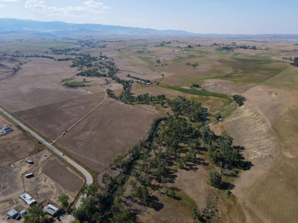 Aerial view of Rock Creek Meadows, a rural landscape with scattered houses, winding roads, patches of trees, and vast open fields under a clear sky.