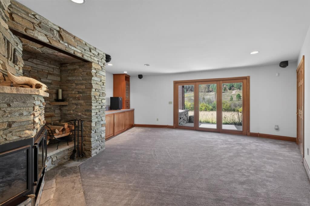 A spacious Elkhorn sanctuary with a carpeted floor, stone fireplace, built-in wooden cabinets, and large glass doors opening to a green landscape. Natural light fills the space.