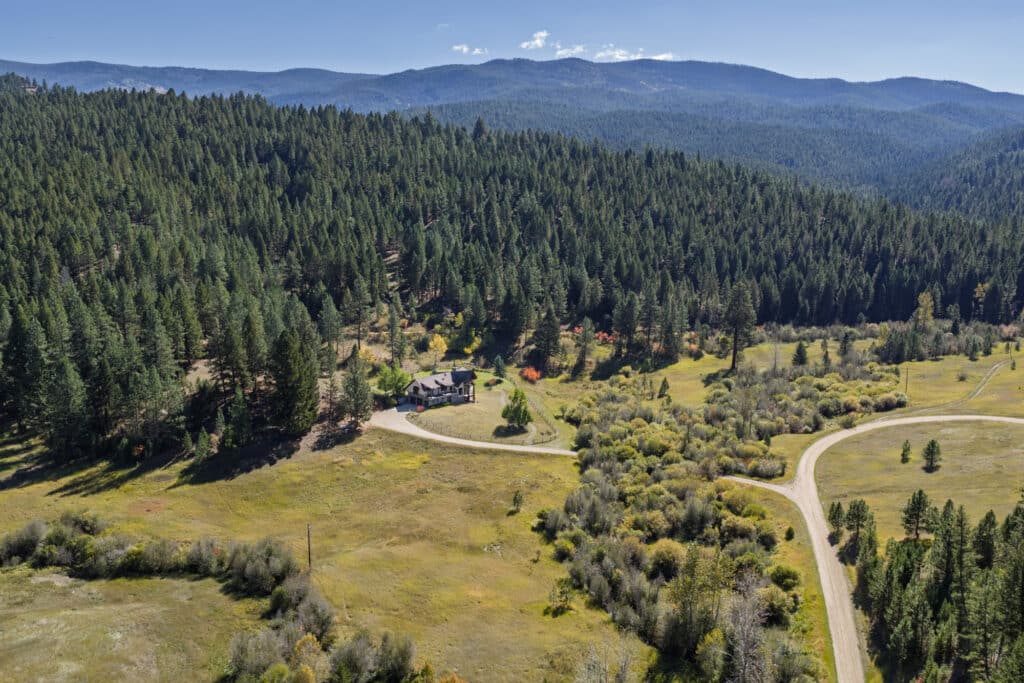 A house sits among trees on a winding road in the lush Elkhorn Sanctuary valley, with mountains in the distance and a clear blue sky above.