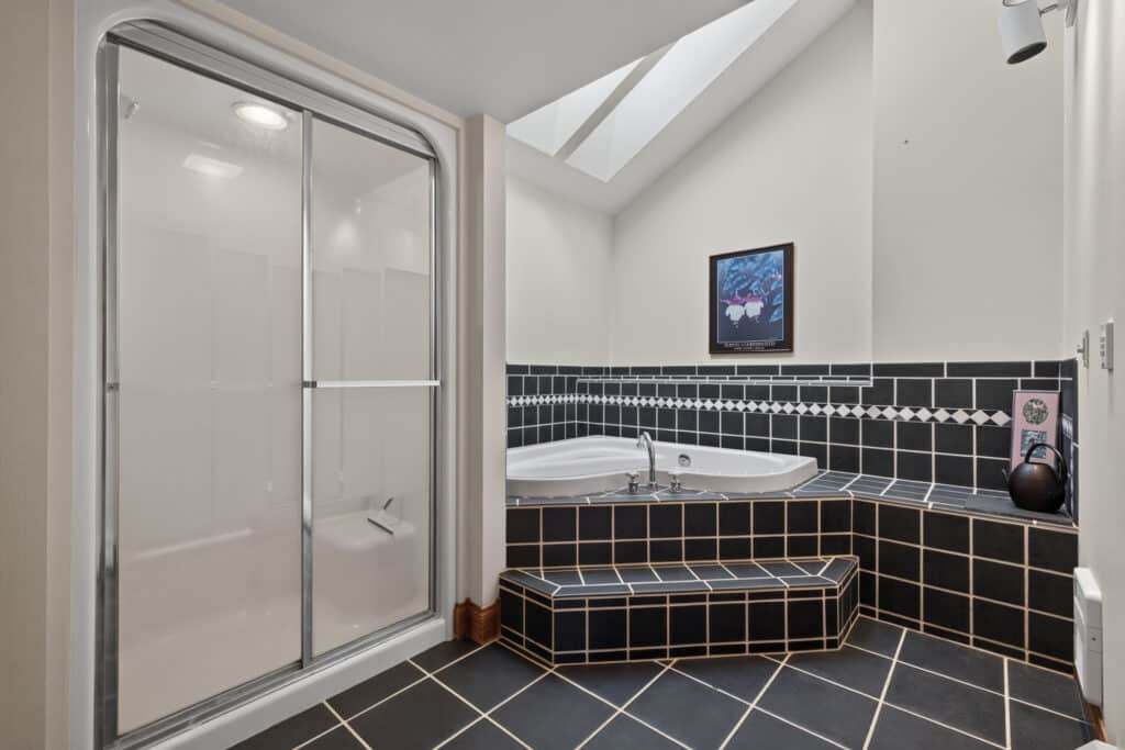 Modern bathroom with black tile, a glass-door shower, a spacious corner bathtub, bench seating, wall art, and a skylight filling this Elkhorn sanctuary with natural light.