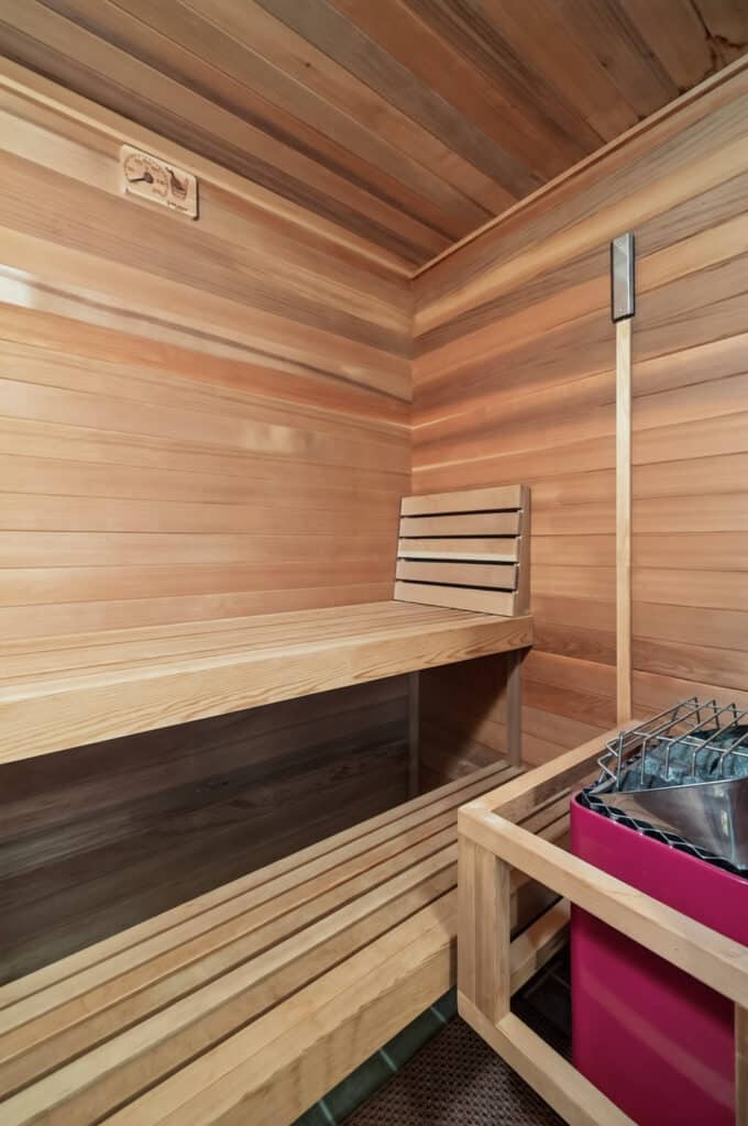 A wooden sauna interior at the Elkhorn sanctuary, featuring tiered benches, a wall-mounted thermometer, and a heater filled with rocks.
