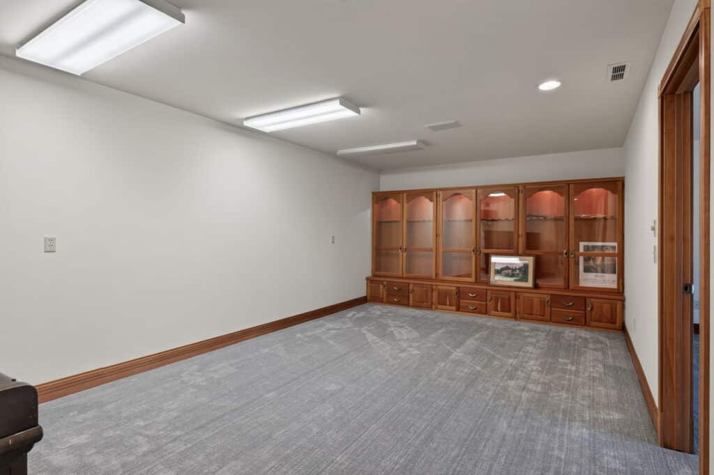 An empty room with gray carpet, white walls, and a large wooden built-in cabinet along the back wall, reminiscent of the tranquil aesthetic of the Elkhorn nature reserve.